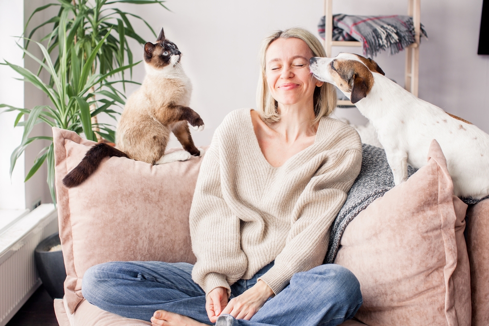 A woman happily spending time with her dog and cat at home, sharing a cozy moment together.