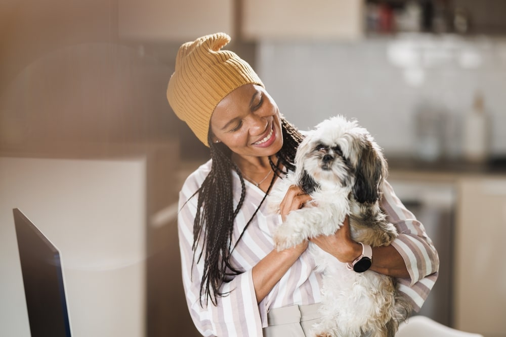 African woman smiling while working at her home office with her dog beside her — preparing for a move from the USA to Belgium.